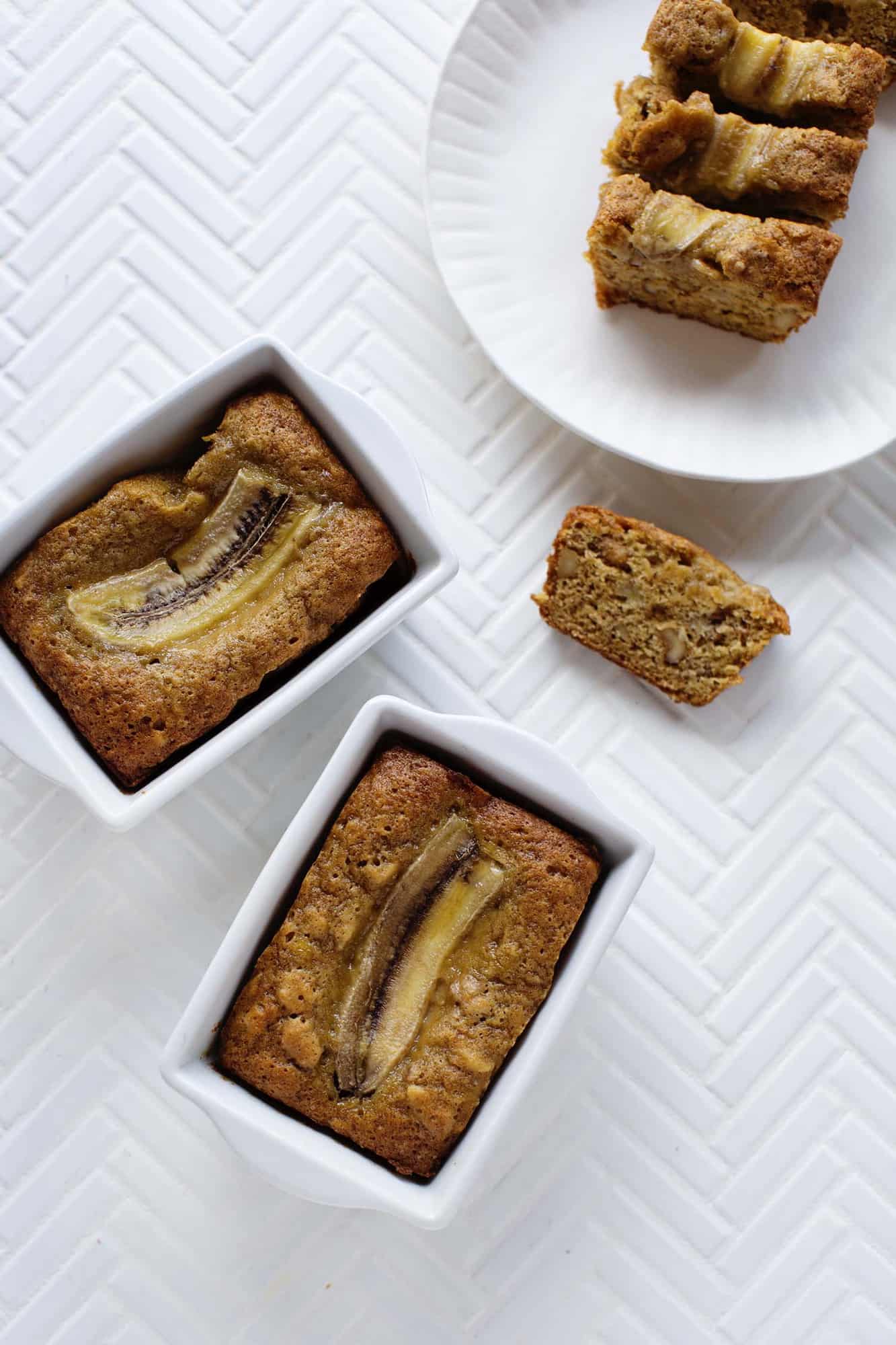 2 loaves of banana bread and 1 loaf of banana bread cut into 4 sections on a plate with 1 piece next to the plate